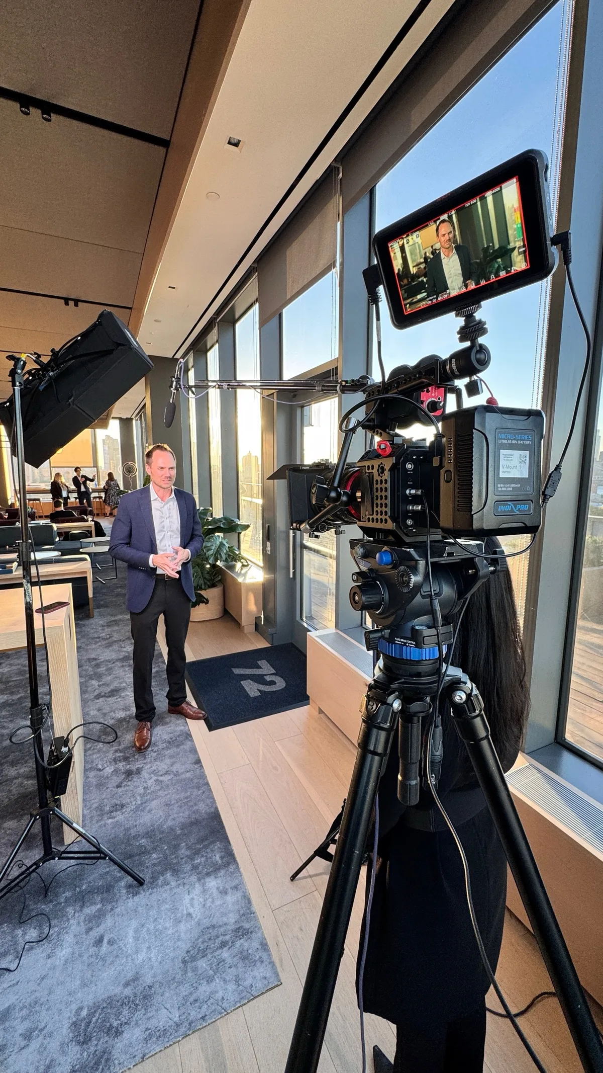 An interview being filmed beside floor-to-ceiling windows, with a cinema camera, monitor and boom microphone in the foreground