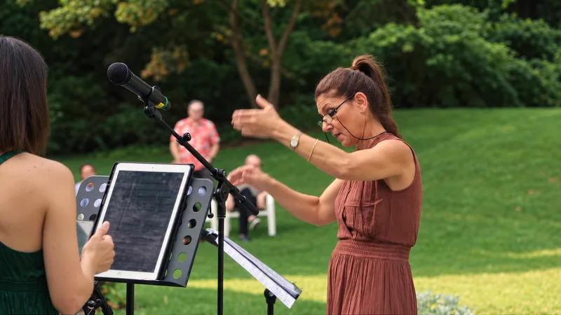 A conductor leading the singers on the lawn during the garden concert