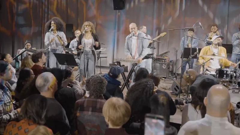 A large band with singers and horns playing to a packed standing crowd