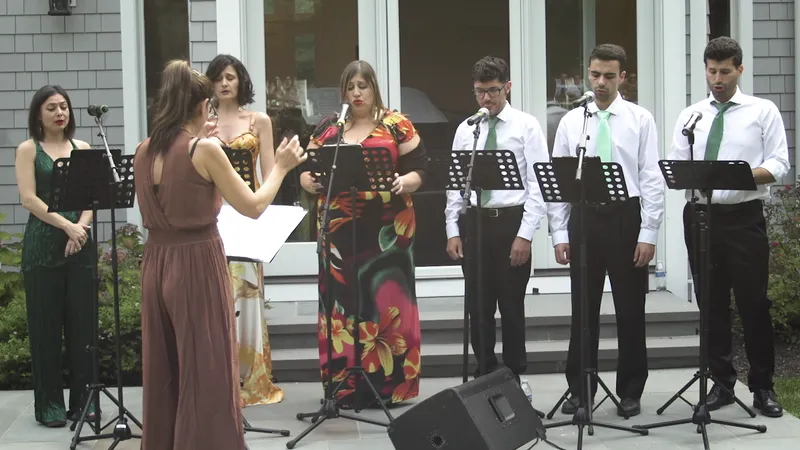 Six singers at music stands on a patio with the conductor in front
