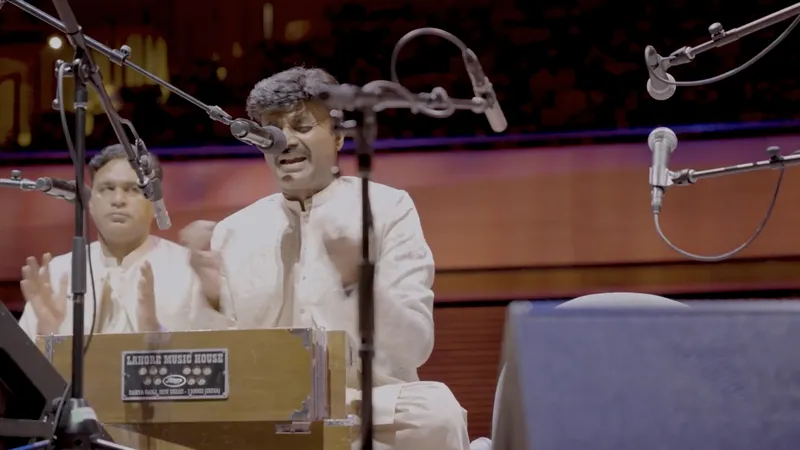 A singer playing harmonium on stage surrounded by microphones