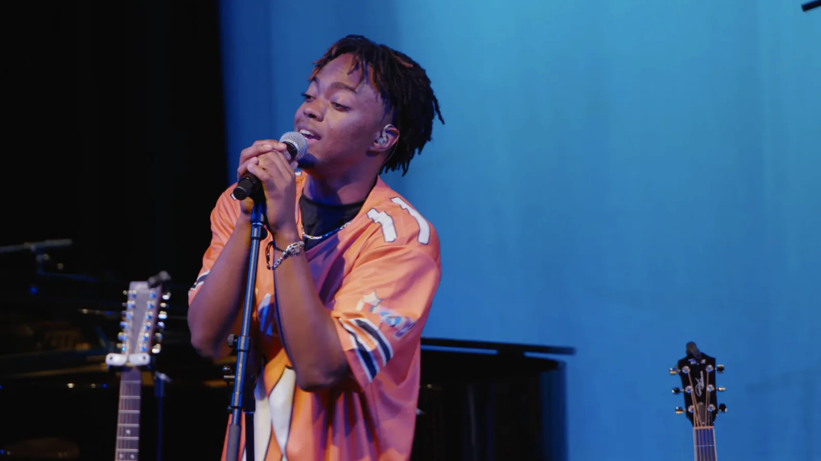 Close-up of a singer in an orange jersey performing at a microphone stand