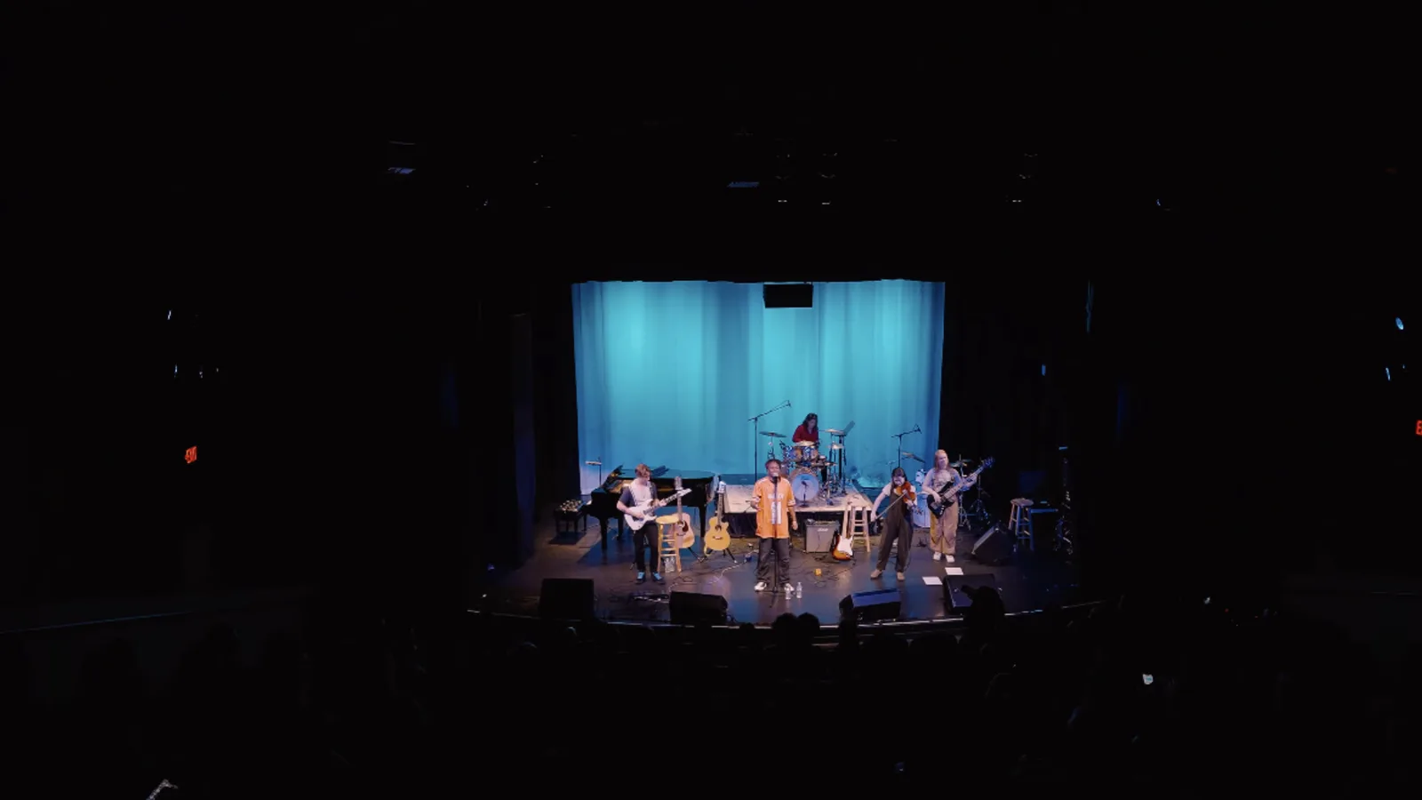 Wide shot from the balcony of a dark theater with a band on a blue-lit stage