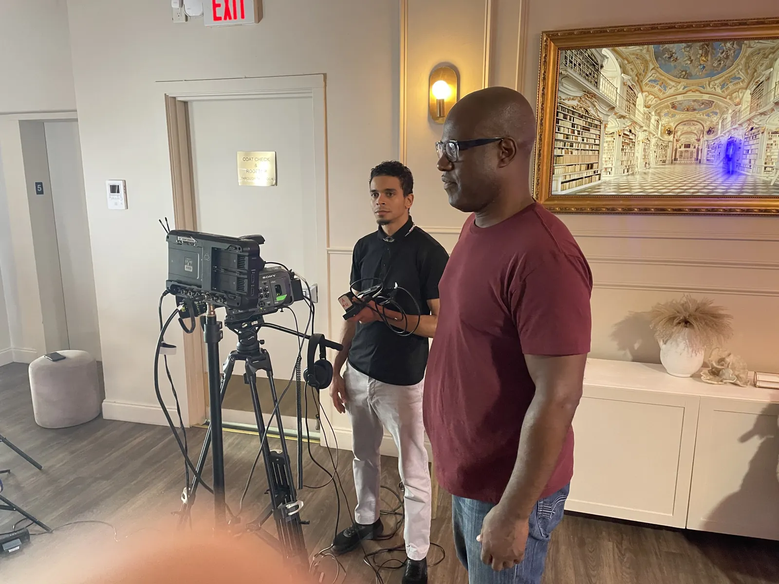 Two crew members standing beside a camera and monitor on set, reviewing a shot