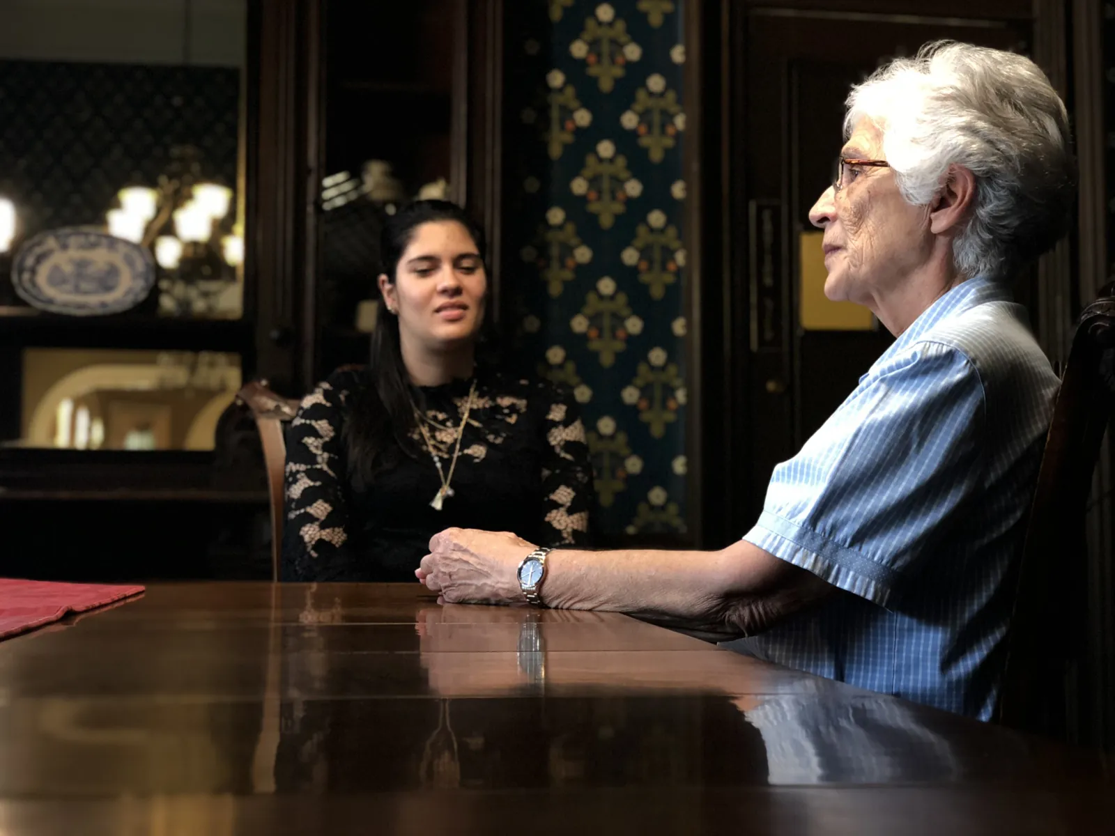 An interviewer and her subject talking across a boardroom table while the crew films
