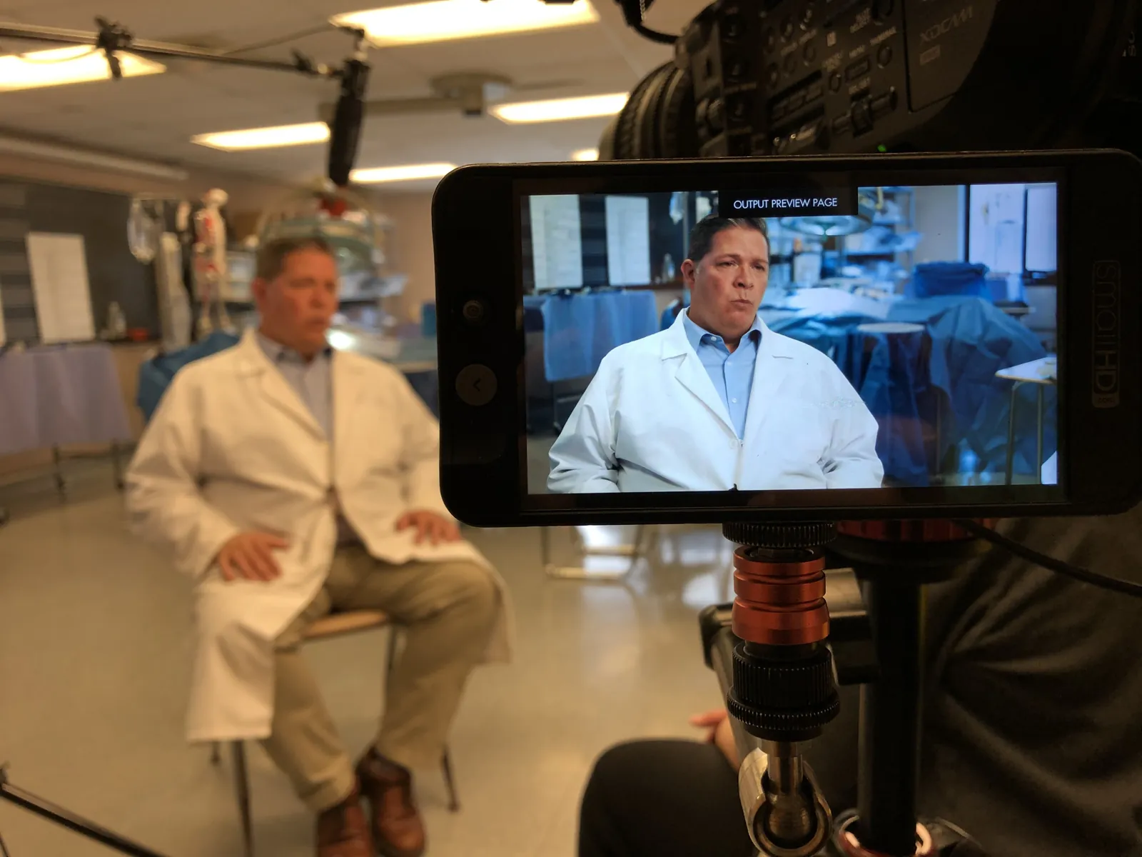 Two physicians in white coats being interviewed, seen on the camera monitor