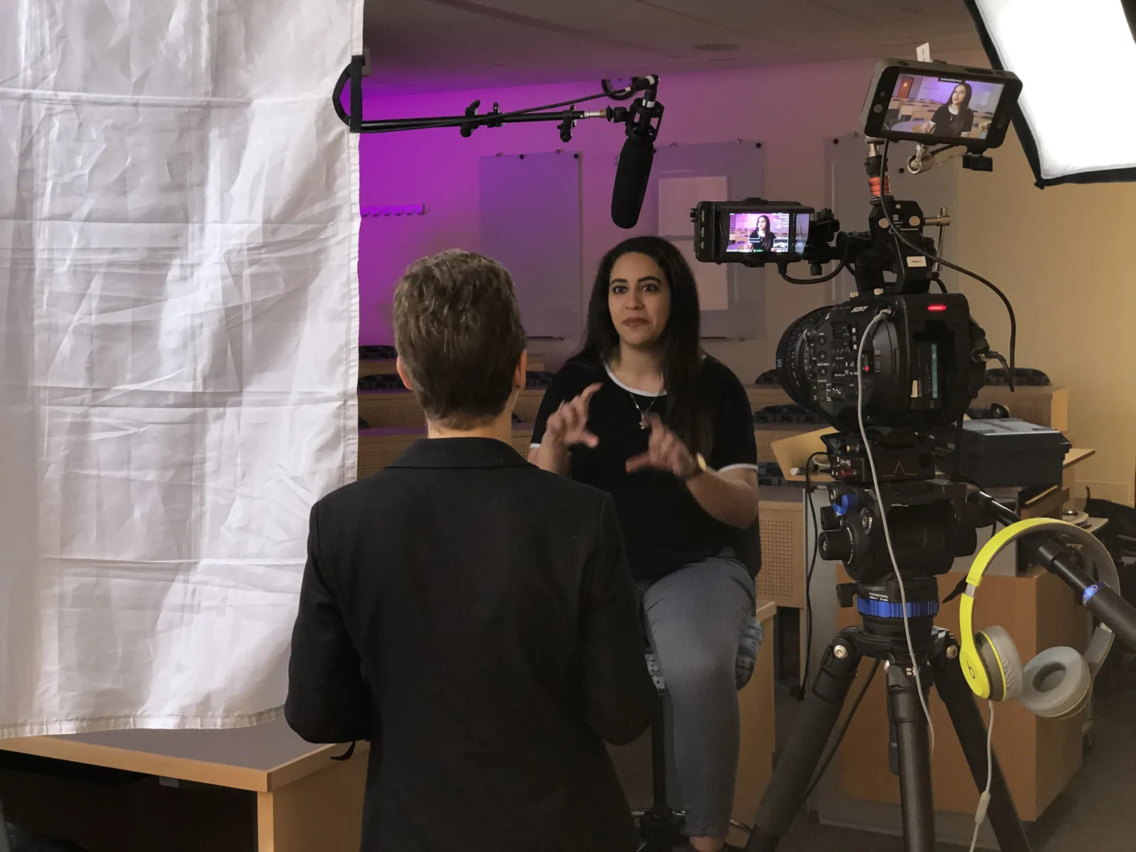 A single-camera interview with a monitor and boom microphone against a white backdrop