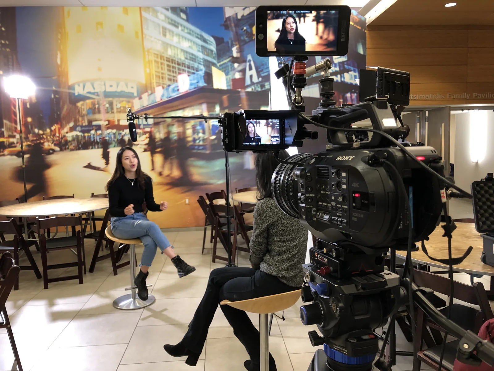 A seated interview filmed against a Times Square backdrop in a New York studio