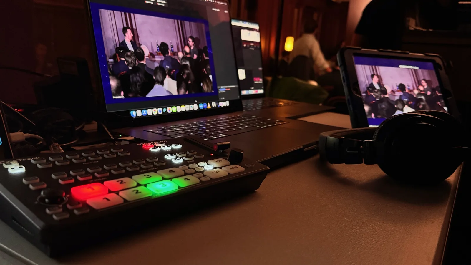A livestream desk with a switcher, a laptop showing the Zoom feed, a tablet and headphones