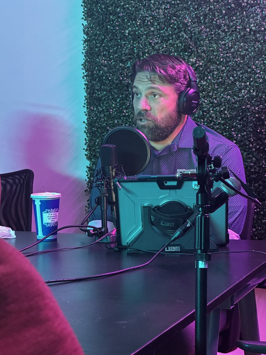 Guest recording a video podcast session at Transcendent Enterprise's Chelsea studio — greenery wall, studio lighting, and multi-microphone setup