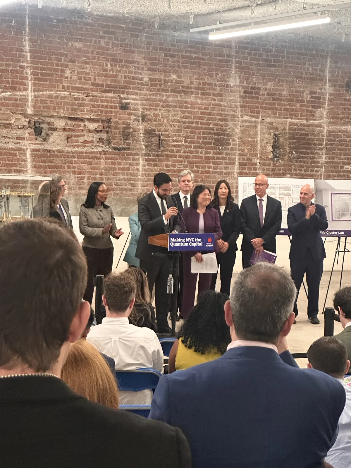 An audience applauding as speakers finish at a podium in front of a brick wall