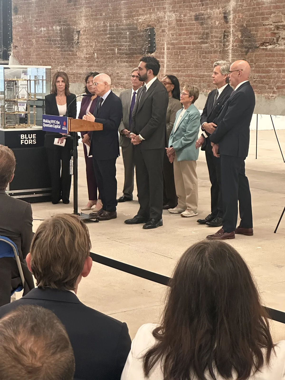 Officials standing behind a podium with a Making NYC the Quantum Capital sign in a brick-walled space