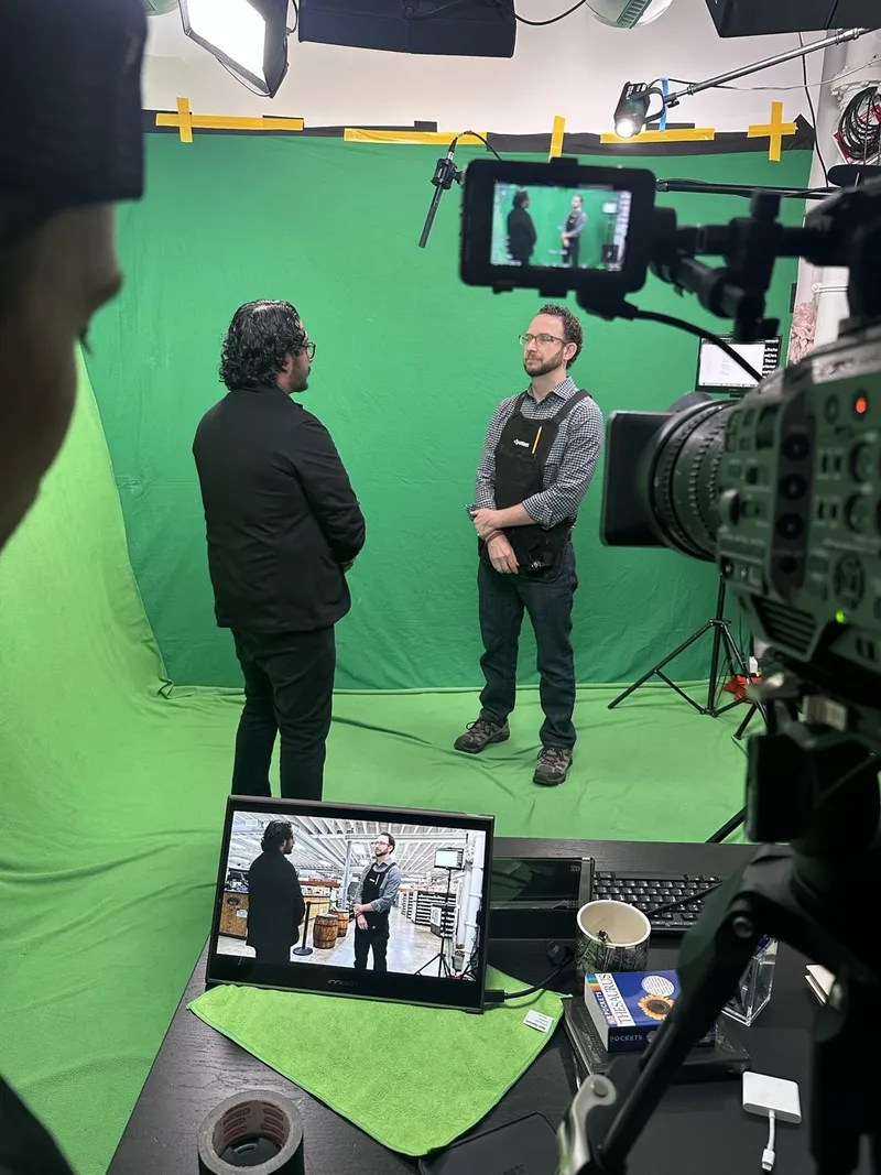 Two people on a green screen while a laptop shows the live composited background