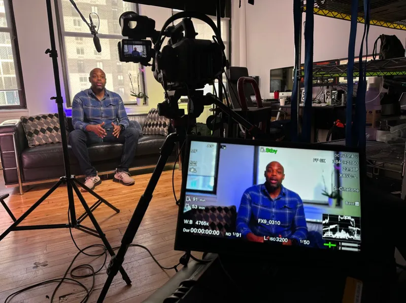 A seated interview subject framed on a large on-set monitor beside the camera