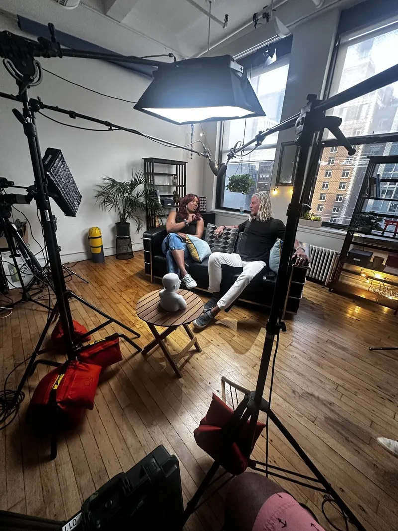 A seated interview being lit and filmed with several lights and stands in a loft studio