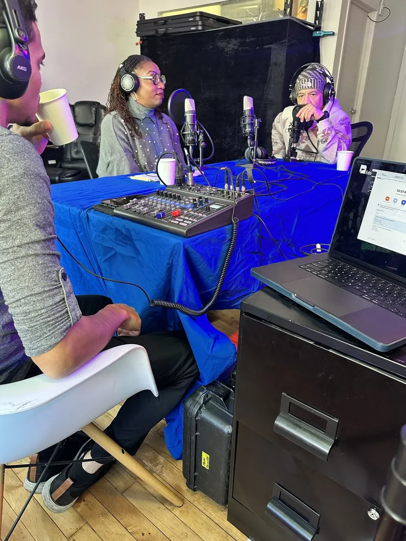 Podcast guests in headphones around a table with microphones, a mixer and a laptop